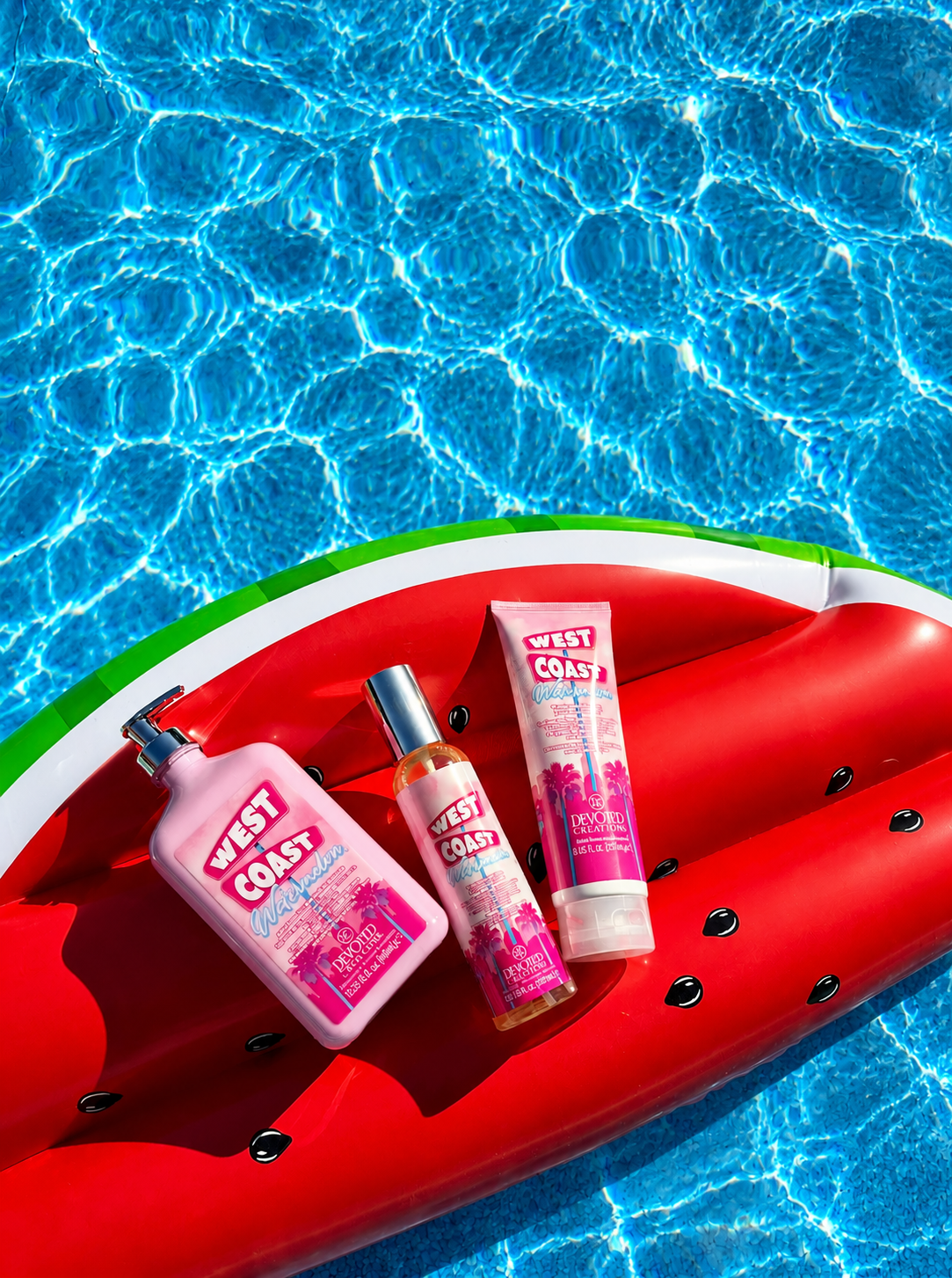 Three West Coast brand body care products in pink packaging are arranged on a red watermelon-shaped float in a swimming pool with blue rippled water visible around them.