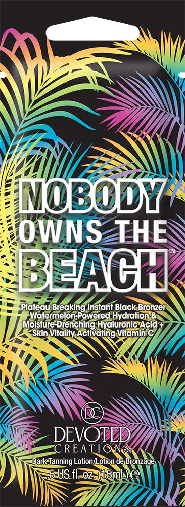 A single use packet of Devoted Creations 'Nobody Owns the Beach' black tanning lotion with a vibrant, multicolored tropical palm leaf pattern on the packaging.
