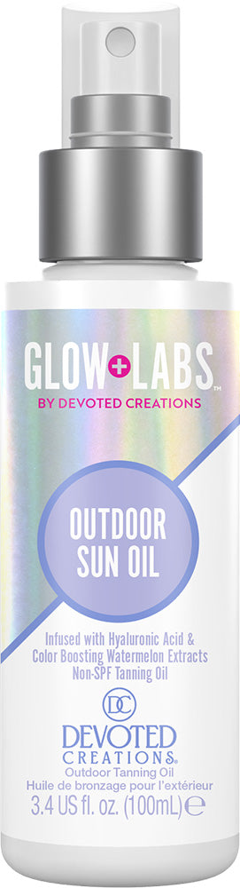 A bottle of Devoted Creations Glow Labs Outdoor Sun Oil, featuring a white and silver spray bottle with a holographic label that displays purple and blue text.