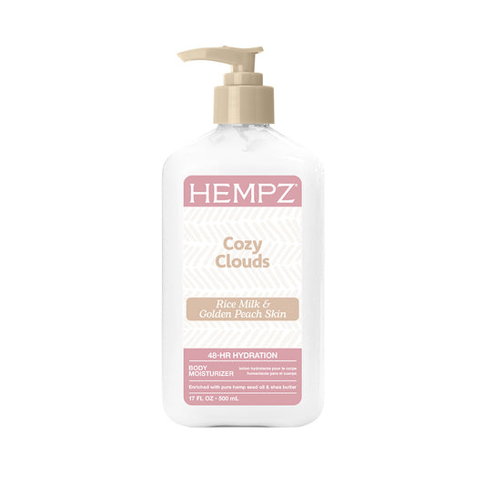 A bottle of Hempz Cozy Clouds body moisturizer, Rice Milk & Golden Peach Skin, featuring a white bottle with a beige pump and pink and beige label details, set against a plain white background.