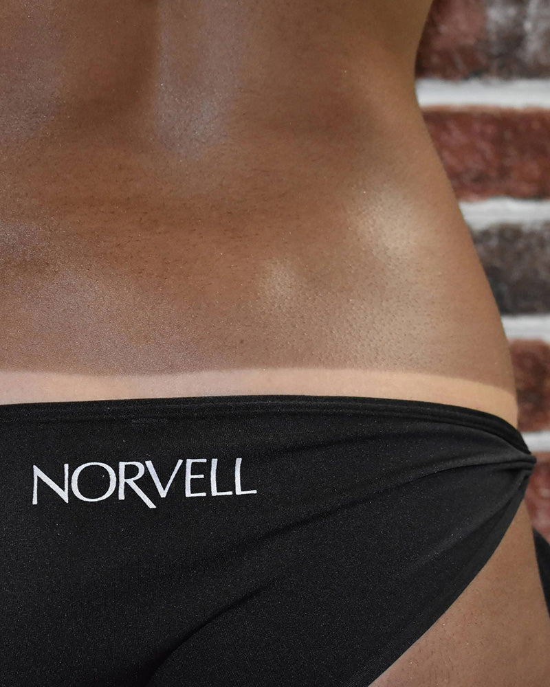 Person wearing black underwear with 'Norvell' branding against a brick wall.